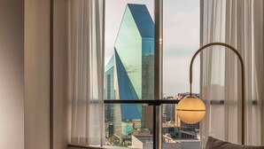 A modern hotel room with a leather sofa, a book titled "David Yarrow," and a view of a cityscape through large windows. - Thompson Dallas, by Hyatt (Dallas)