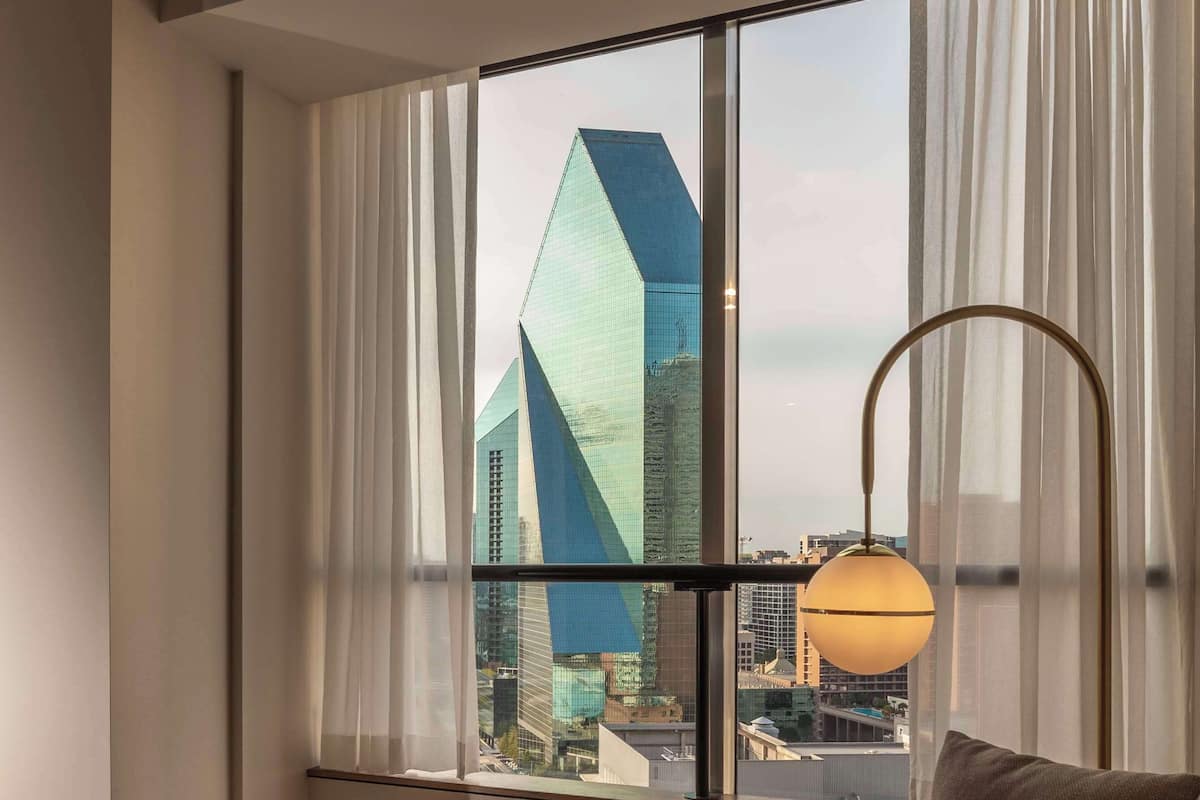 A modern hotel room with a leather sofa, a book titled "David Yarrow," and a view of a cityscape through large windows.