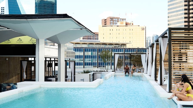 A swimming pool with a view of modern buildings, including a distinctive glass structure. - Thompson Dallas, by Hyatt (Dallas)