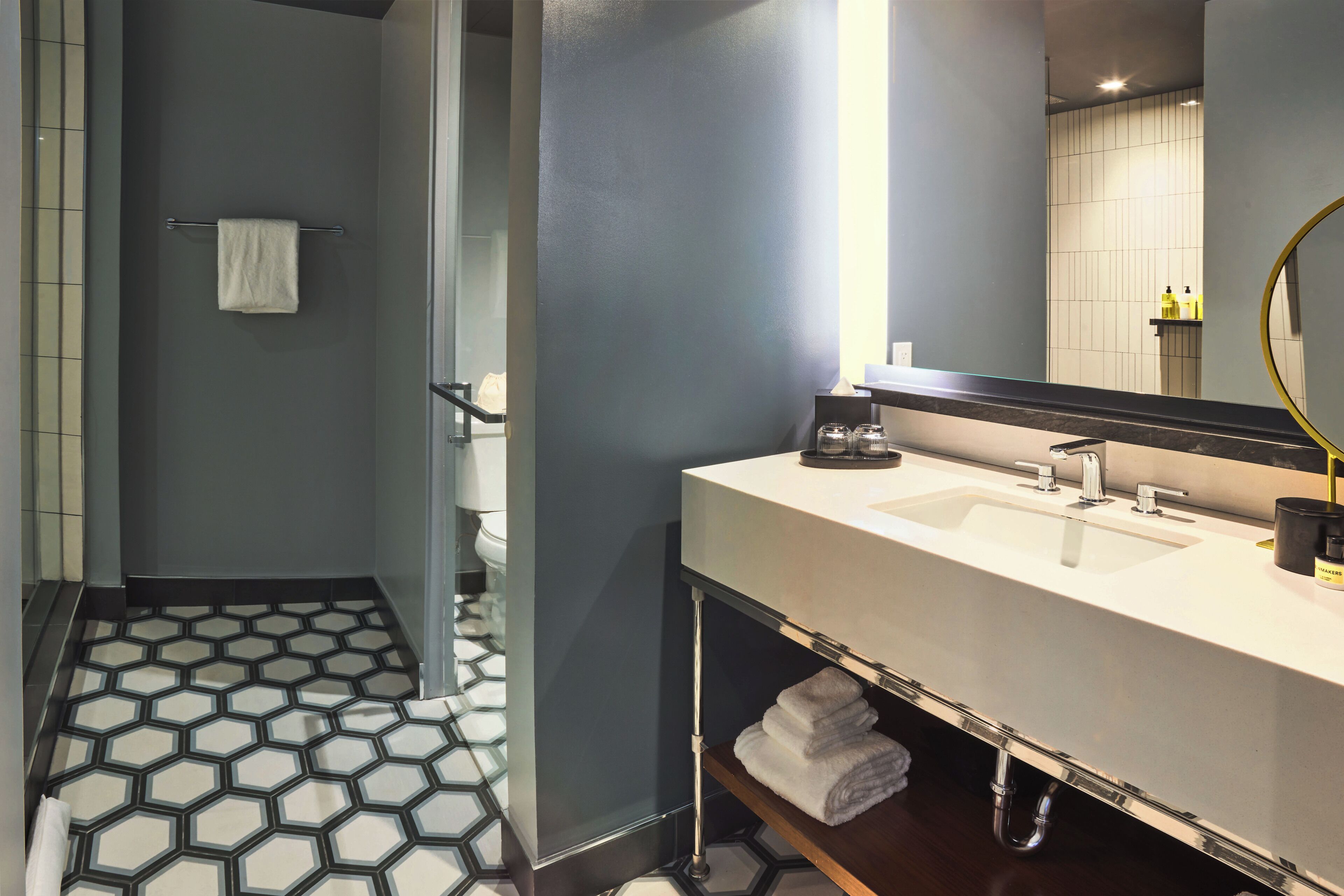 A modern bathroom with a large mirror, dual sinks, and a hexagonal patterned floor.