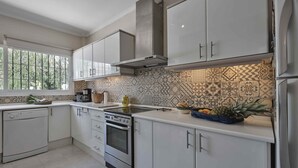 A modern kitchen with white cabinets, a stainless steel oven, and a patterned backsplash. - Villa Pinsapo (Benahavís)
