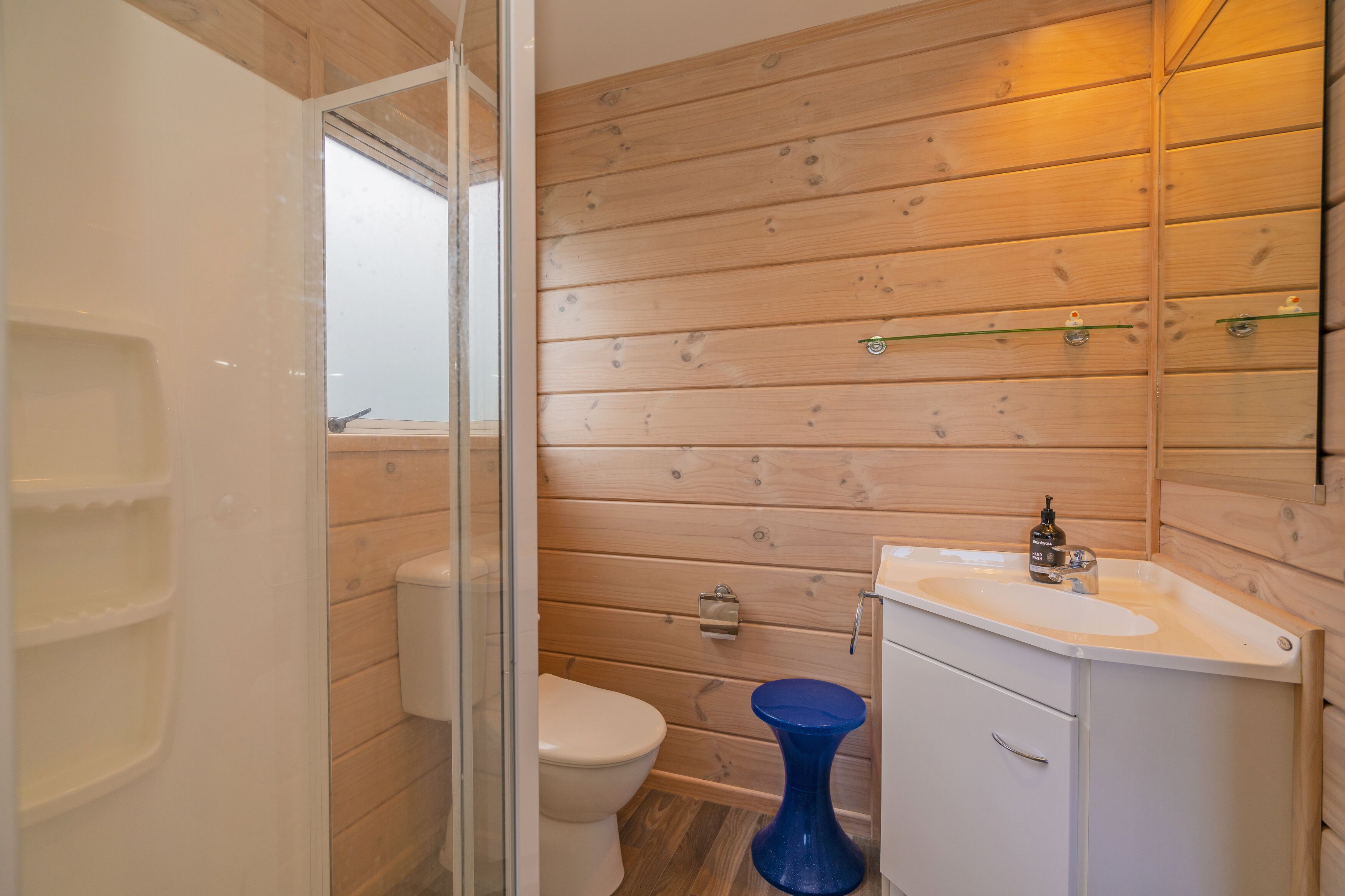 A bathroom with wooden paneling, a white toilet, a blue bidet, and a white sink with a mirror above it.