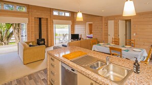 A modern kitchen with granite countertops, a sink, and a dining area with a table and chairs. - Opoutere Oasis - Opoutere Holiday Home (Opoutere)