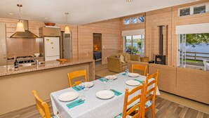 A modern kitchen with a stove, refrigerator, and dining area set for six. - Opoutere Oasis - Opoutere Holiday Home (Opoutere)