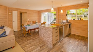 A cozy cabin interior with a dining area, kitchen, and a sofa. - Opoutere Oasis - Opoutere Holiday Home (Opoutere)