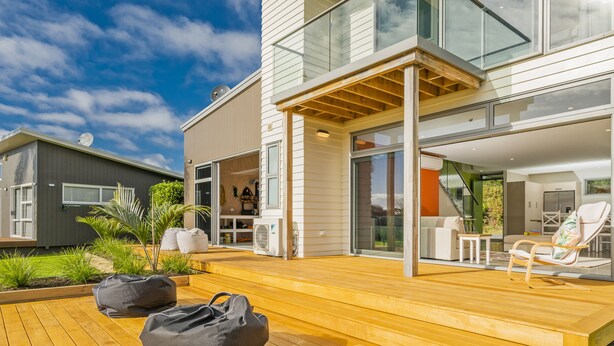 Une maison moderne dotée d’une terrasse en bois, d’une porte vitrée donnant sur l’espace de vie et d’une antenne parabolique sur le toit.