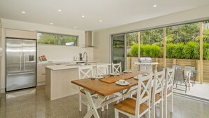Une cuisine moderne dotée d’un réfrigérateur en acier inoxydable, d’un four encastré et d’un coin repas avec une table en bois et des chaises blanches.