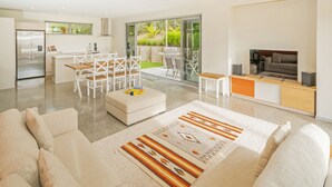 Un espace de vie moderne comprenant une cuisine, un coin repas et un espace salon confortable avec un canapé et un pouf.