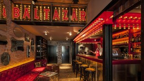 Zona de bar con un letrero de neón rojo, asientos de cuero y un barman.