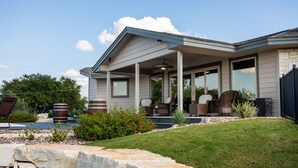 Een modern huis met een overdekte veranda, zitplaatsen buiten en een aangelegde tuin.