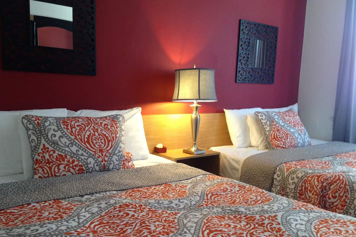 A hotel room with two beds, each with patterned bedding, a nightstand with a lamp, and a mirror on the wall.