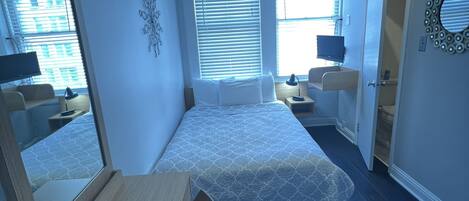 A bedroom with a bed, a desk, a chair, a mirror, and a ceiling fan.
