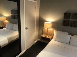 A hotel room with two beds, a nightstand with a lamp, a mirror, and artwork on the wall.