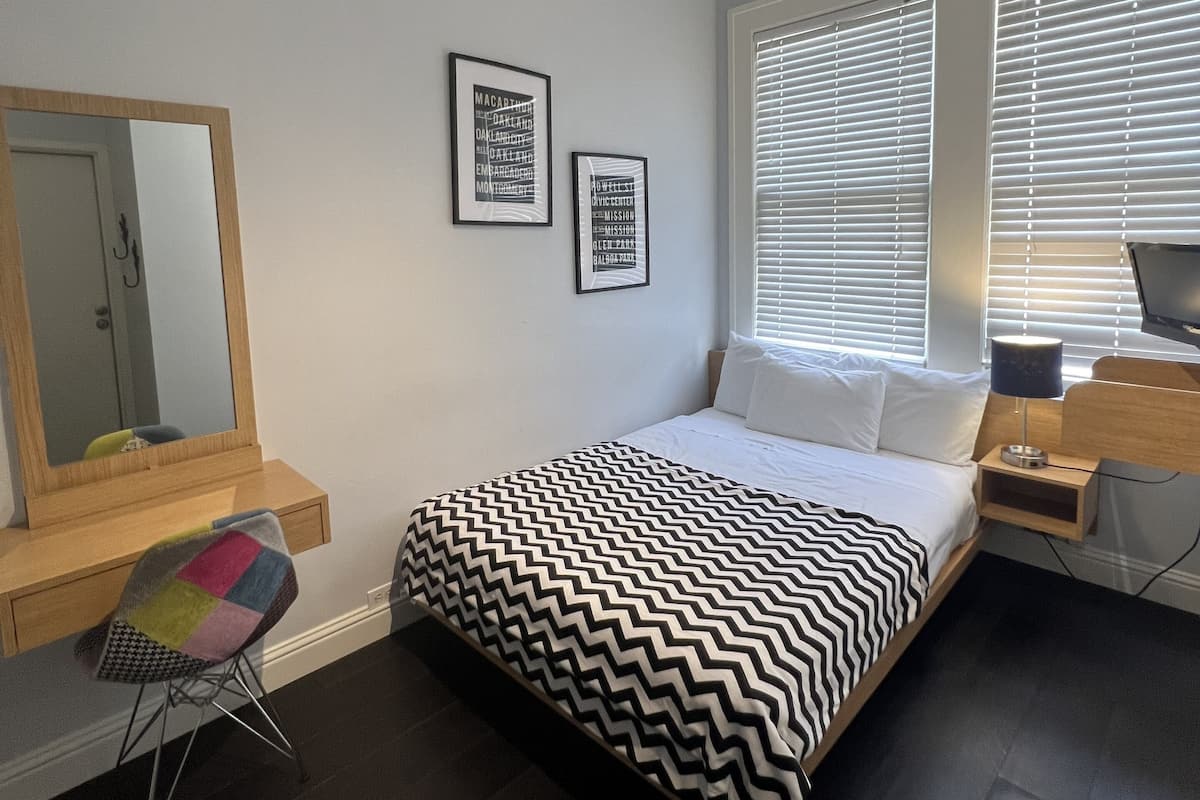 A modern bedroom with a bed, a chair, a desk, and a window with blinds.