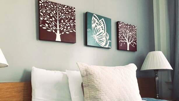 A hotel room with a bed, two pillows, a blue blanket, and three wall art pieces depicting trees and a butterfly. - Touchstone Hotel - City Center (San Francisco)