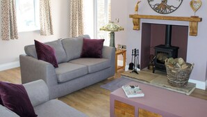 Ein gemütliches Wohnzimmer mit grauem Sofa, violetten Kissen, einem Kamin und einer dekorativen Wandgestaltung mit Baum.