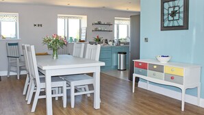 Eine moderne Küche mit weißen Schränken, ein Essbereich mit einem weißen Tisch und Stühlen sowie eine dekorative Uhr an der Wand.