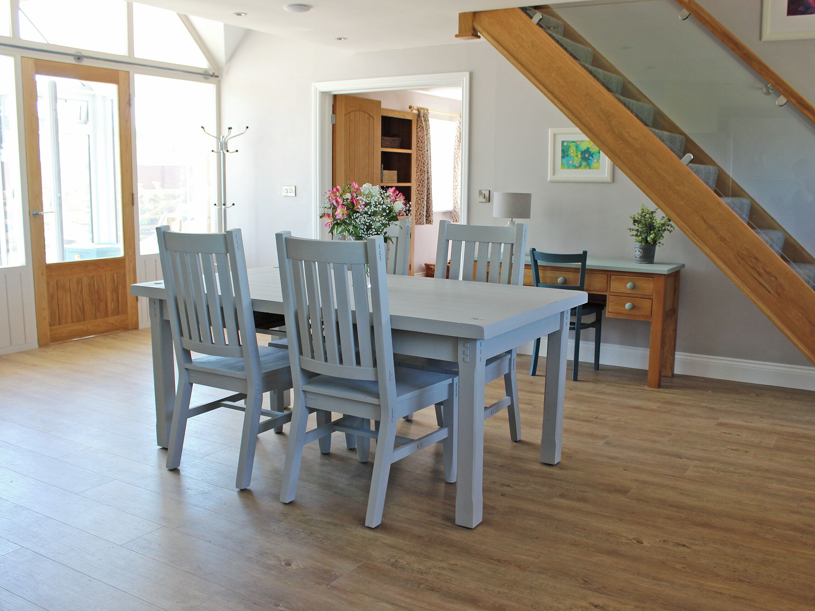 A dining area with a wooden table and chairs, a small desk with a chair, and a staircase.