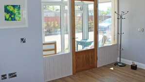 Ein Zimmer mit Holztür, Kleiderhaken, einem gerahmten Bild und einem Fenster mit Blick ins Freie.