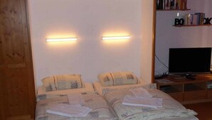 Una cama doble con dos mesitas de noche, un televisor de pantalla plana y una estantería con libros.