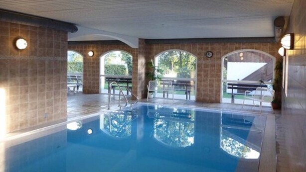 Una piscina interior con paredes de azulejos y una solárium de madera.