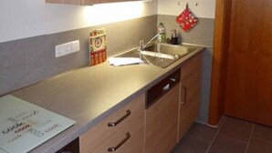 Una cocina con armarios de madera, un lavamanos de acero inoxidable y salpicadero de azulejos.