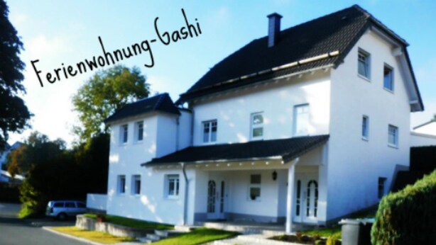 Una casa de dos pisos con fachada blanca y techo oscuro.