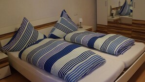 Cama doble con ropa de cama a rayas y almohadas combinadas, mesita de noche con lámpara y espejo en la pared.