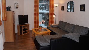 Una sala de estar con un sofá, una mesa de centro, un televisor y una ventana con cortinas.