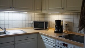 Cocina con armarios blancos, microondas, cafetera y lavabo.