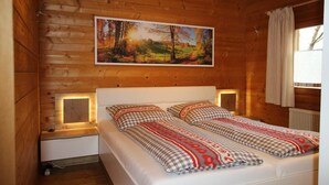 A wooden cabin room with a bed, a painting, and a window with curtains. - Blockhaus Noffke (Stamsried)