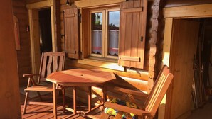 A wooden deck with a table and chairs, a window with shutters, and a door. - Blockhaus Noffke (Stamsried)