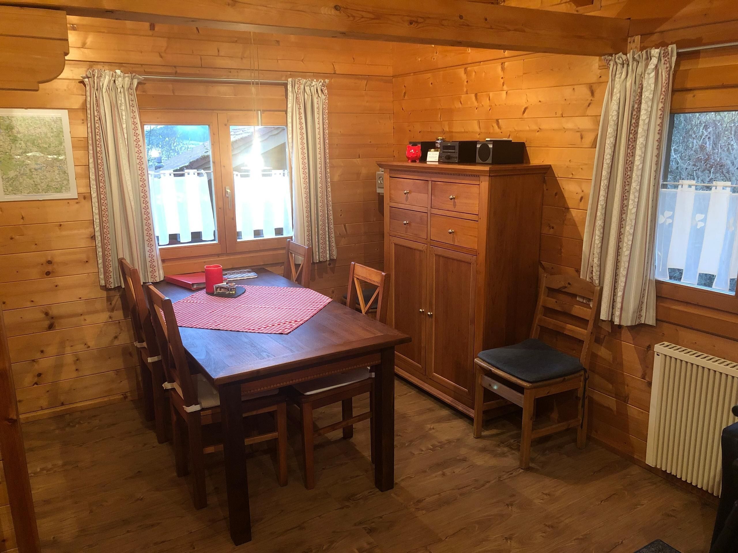 A wooden cabin with a dining table, chairs, a cabinet, and a radiator.