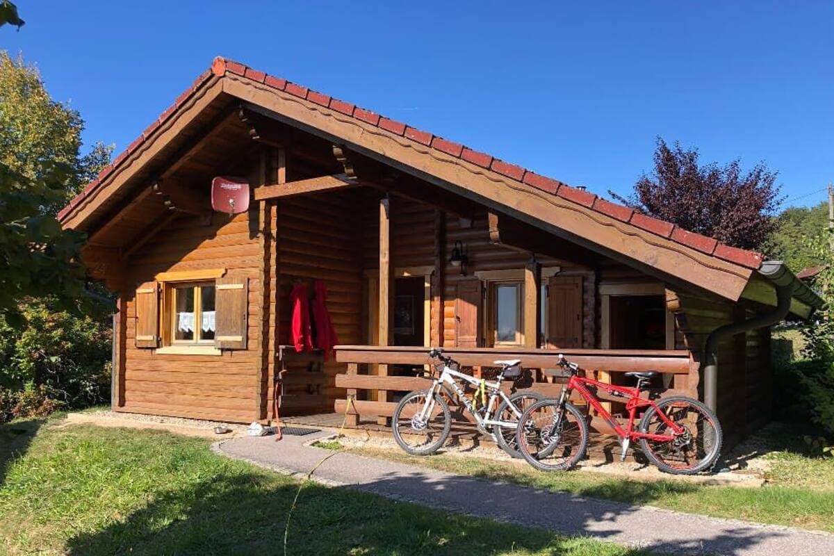 Una cabaña de madera con un porche, dos bicicletas y una chaqueta roja colgada en la puerta.