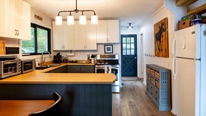 A kitchen with wooden countertops, white cabinets, a central island, and a black door. - Adorable 3Bed, 2Bath Cottage and Garage Lounge! Grassy Lawns! Kayaks! (Rosseau)