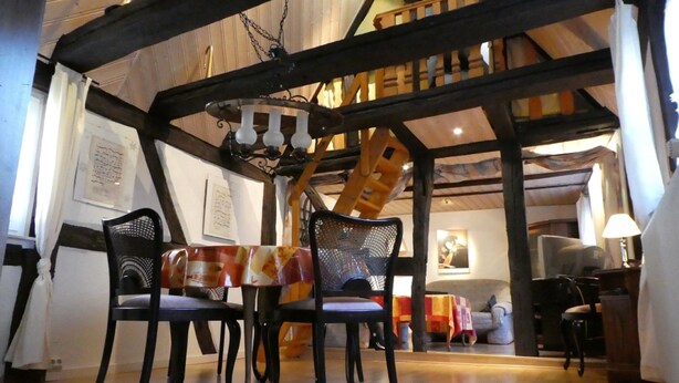 Uma sala de jantar com mesa e cadeiras de madeira, uma escada e um ambiente acolhedor.