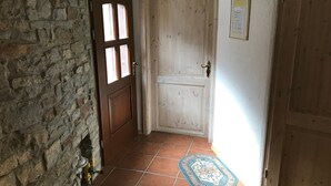 Um corredor com parede de pedra, porta de madeira com painéis de vidro, piso ladrilhado e tapete.