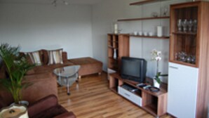 Uma sala de estar com um sofá marrom, uma mesa de centro, uma TV em um suporte de madeira e um armário com copos.