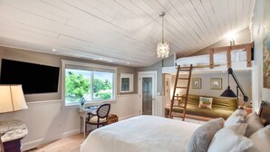 Un dormitorio con una cama litera, un escritorio con silla, una araña y una ventana con vistas a vegetación.