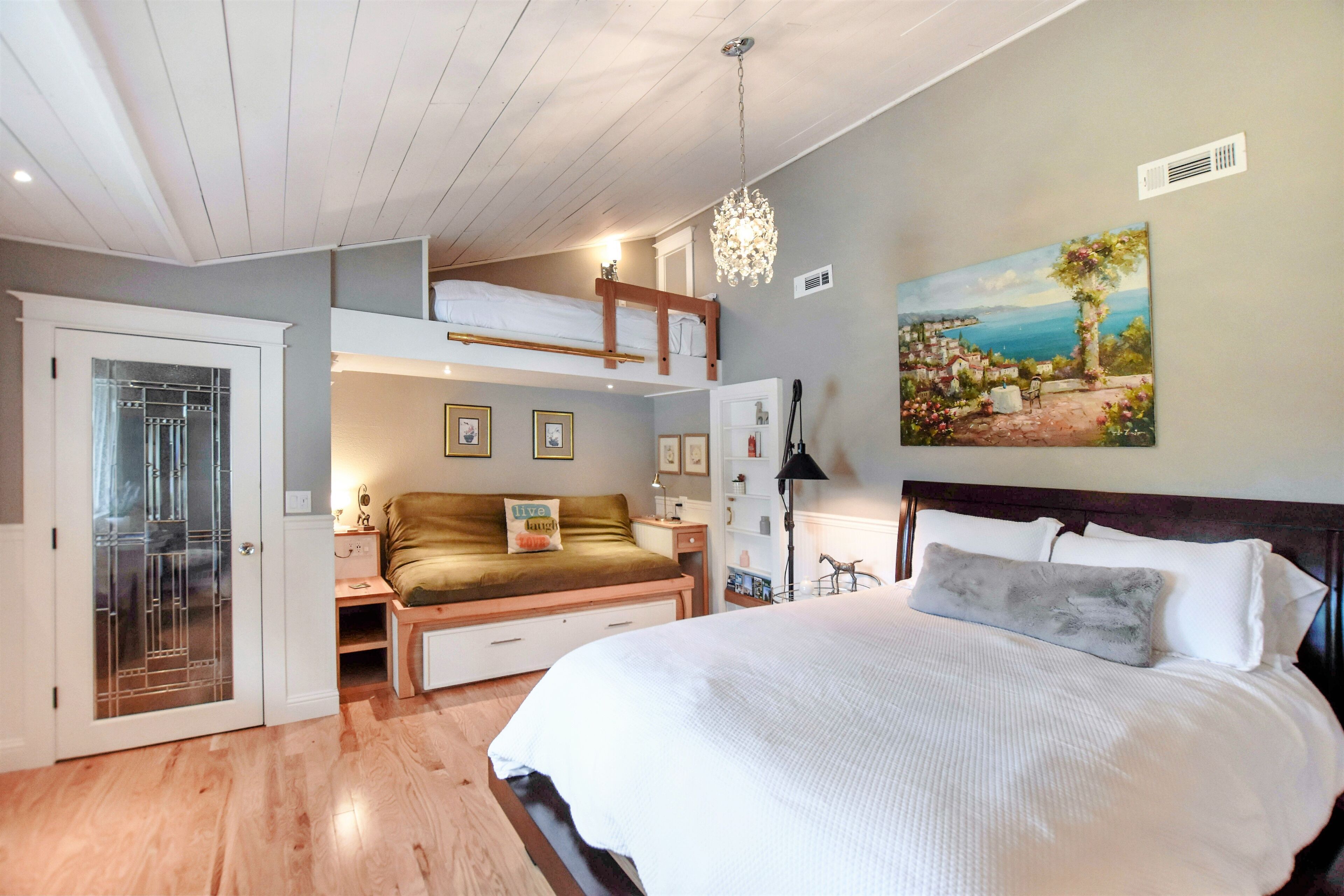 Een slaapkamer met een stapelbed, een groot bed, een bureau en een schilderij aan de muur.