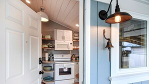 Cocina compacta con muebles blancos, microondas, horno y pileta. Se observa una ventana con vista al exterior.