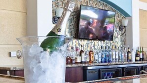 A bar area with a large TV screen, a variety of liquor bottles, and a glass pitcher filled with ice and a bottle of champagne. - Orlando Resort Across from Universal Epic Universe (Orlando)