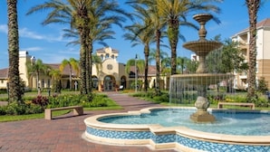 A courtyard with a fountain, palm trees, and a building with a clock tower. - Orlando Resort Across from Universal Epic Universe (Orlando)