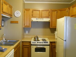 A compact kitchen with wooden cabinets, a stove, a refrigerator, and a wall clock. - Sugar Ski & Country Club Unit 231 Silver (Banner Elk)