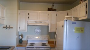 A kitchen with white cabinets, a stove, a refrigerator, and a clock on the wall.
