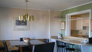 A dining area with a marble table, black leather chairs, a chandelier, and a kitchen visible through an open doorway.