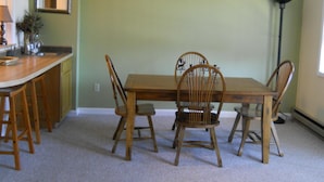 A dining area with a wooden table and chairs, a kitchen counter, a ceiling fan, and a decorative wall piece.