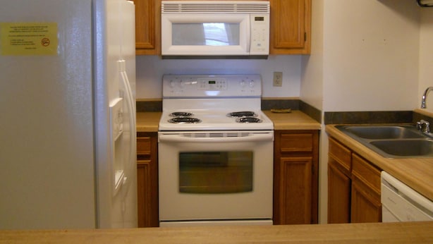 A kitchen with wooden cabinets, a white refrigerator, a microwave, a stove, and a sink.
