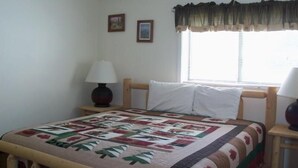 A bedroom with a wooden bed, a quilt, a window with blinds, and two framed pictures on the wall.