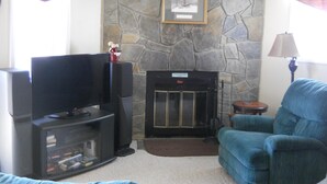 A living room with a stone fireplace, a television, and a blue armchair. - Sugar Ski & Country Club Unit 436 Silver (Banner Elk)